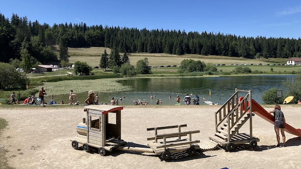 Um parque à beira do lago com um parquinho, incluindo um escorrega e uma casinha.