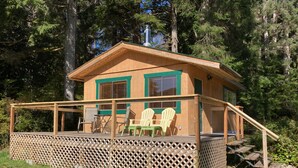 A wooden cabin with a deck, two Adirondack chairs, and a small table. - Ocean Front wilderness Cabin, brand new - Spa bathroom, fully equipped Kitchen (Quatsino)