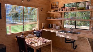 A wooden cabin kitchen with a dining table, chairs, a sink, and various kitchen appliances. - Ocean Front wilderness Cabin, brand new - Spa bathroom, fully equipped Kitchen (Quatsino)