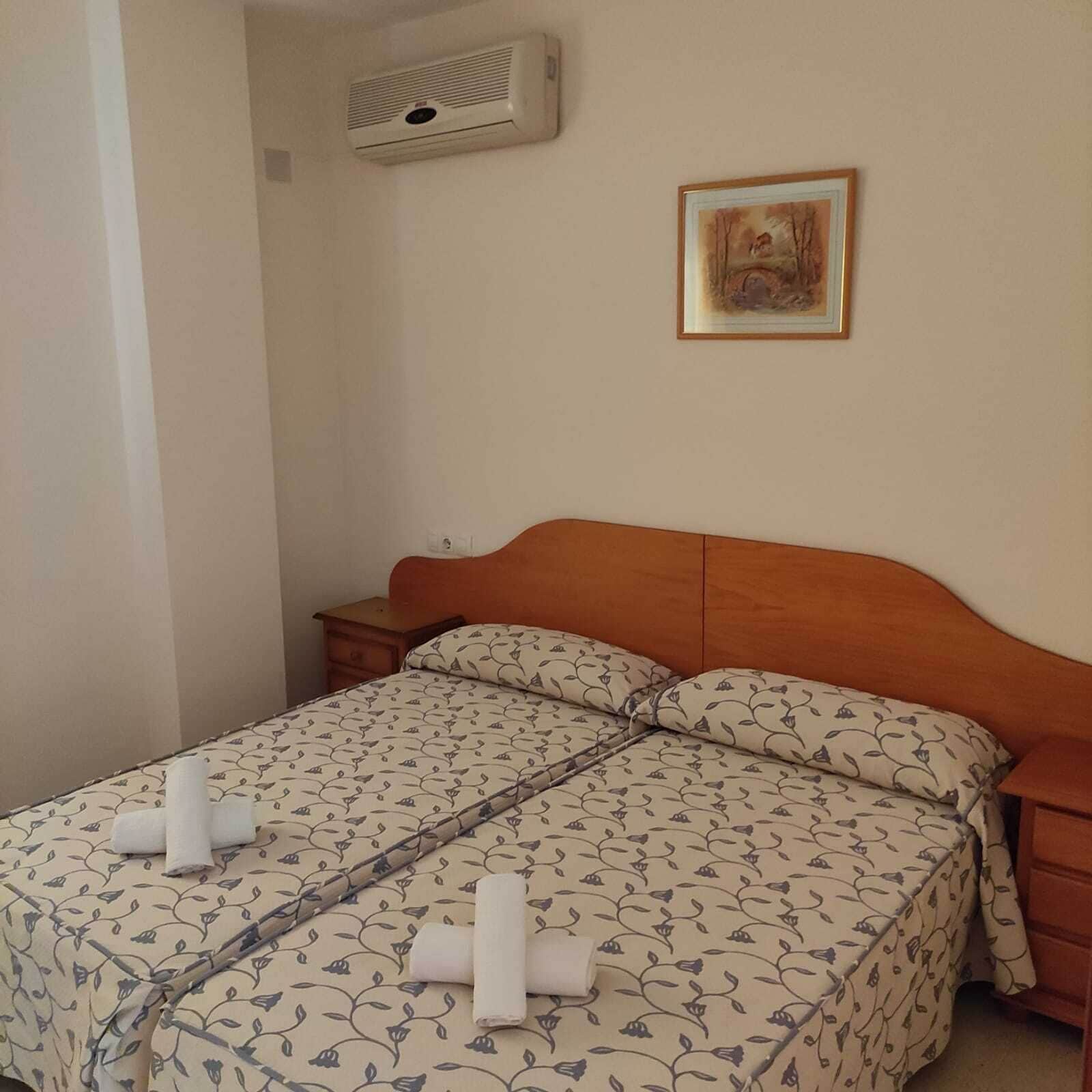 A double bed with floral bedding, a wooden headboard, and a small bedside table.