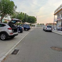 Calle con coches aparcados y un edificio con entrada protegida por una reja.
