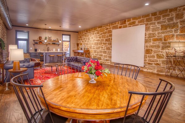A spacious living area with a round wooden dining table, comfortable seating, a stone wall, and a kitchen in the background. - The Loft On The Square (Mason)