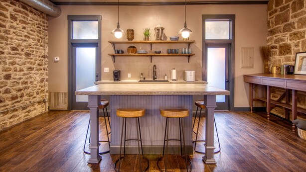 Una cocina con una isla grande, taburetes de bar, lámparas colgantes y una pared de acento de piedra.