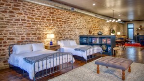 Una habitación con dos camas, un banco de madera, una estantería y un rincón comedor con una alfombra roja.