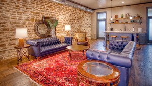 Un moderno salón con pared de piedra, sofás de cuero, alfombra estampada y una zona de bar con taburetes y estanterías.