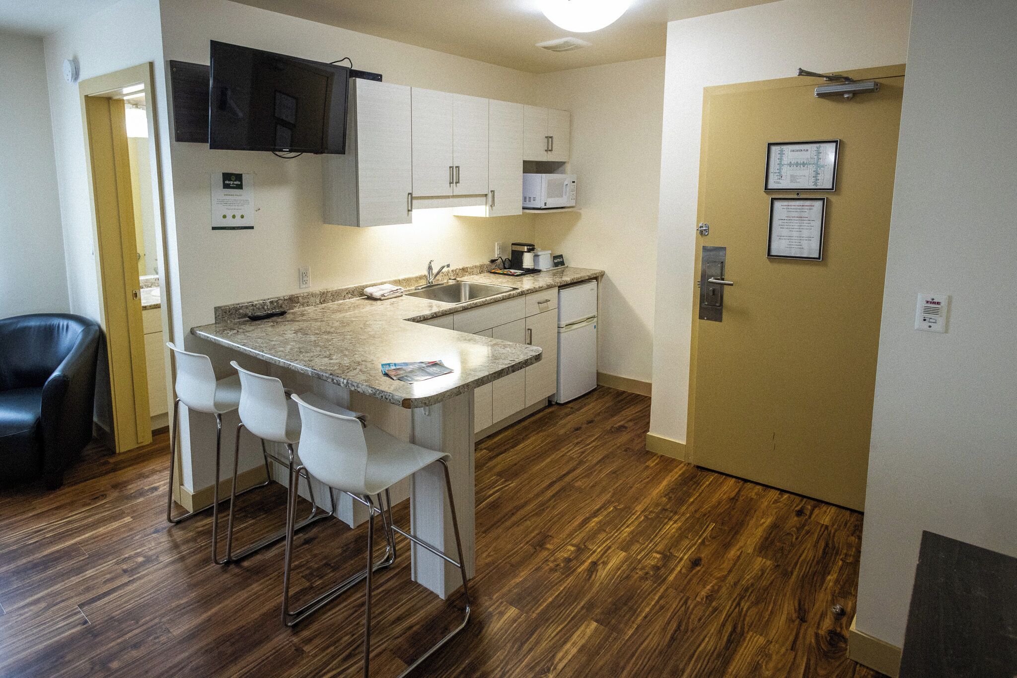 A compact kitchen with a sink, microwave, and bar stools.