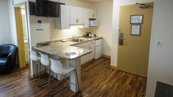 A compact kitchen with a sink, microwave, and bar stools.