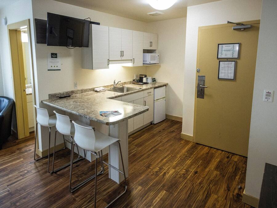A compact kitchen with a sink, microwave, and bar stools.