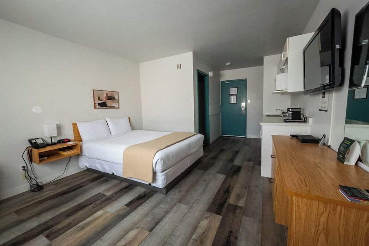 A hotel room with a bed, bedside table, desk, and a television.