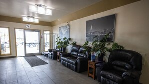 A lobby with a reception desk, black leather sofas, potted plants, and a large cityscape painting on the wall. - Sleep Suite Motel (Steinbach)