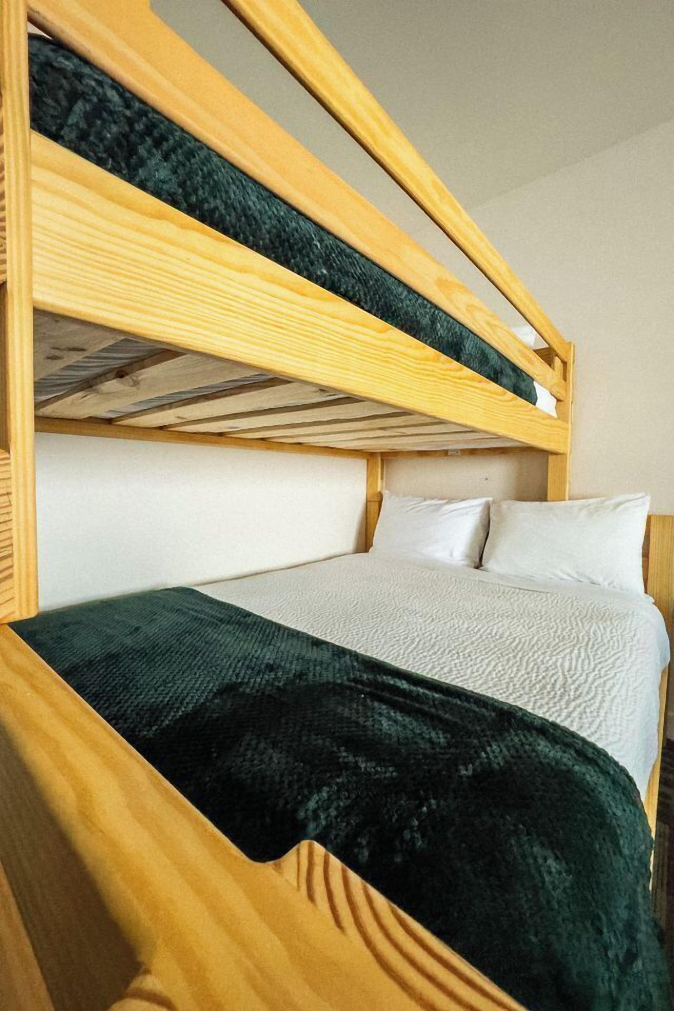 A bunk bed with a wooden frame, a white mattress, and a green blanket.