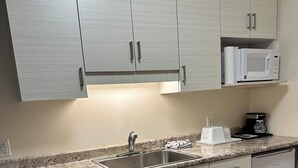 A modern kitchen with light grey cabinets, a stainless steel sink, a microwave, and a coffee maker. - Sleep Suite Motel (Steinbach)