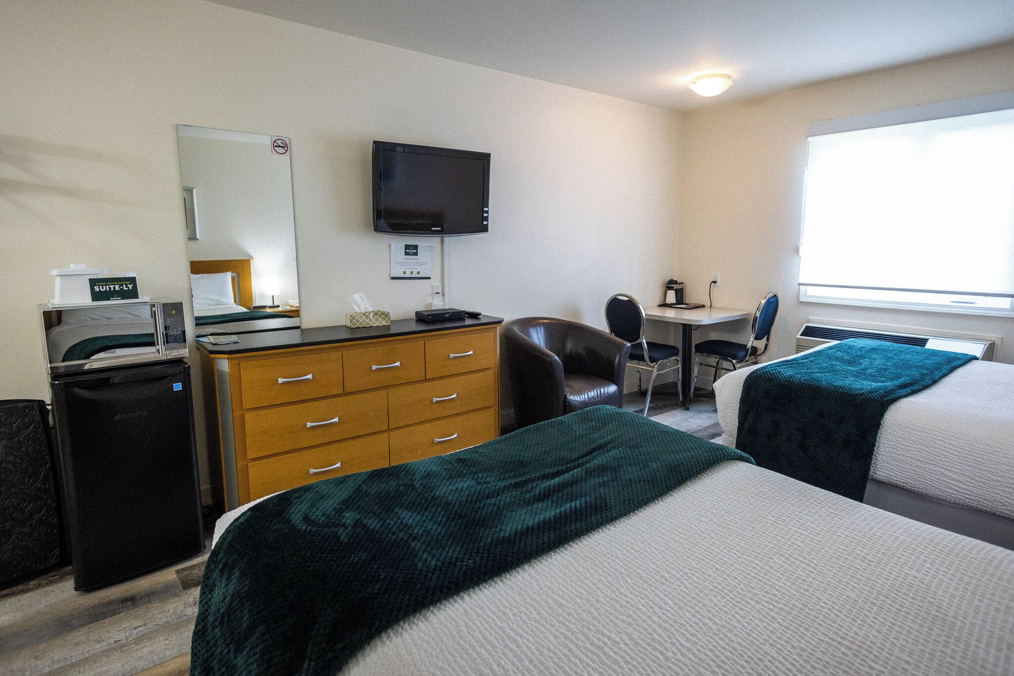 Een hotelkamer met twee bedden, een bureau, een stoel, een televisie, een minibar en een raam.