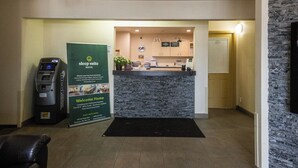 A reception area with a stone wall, a reception desk, a digital kiosk, and a welcome sign. - Sleep Suite Motel (Steinbach)