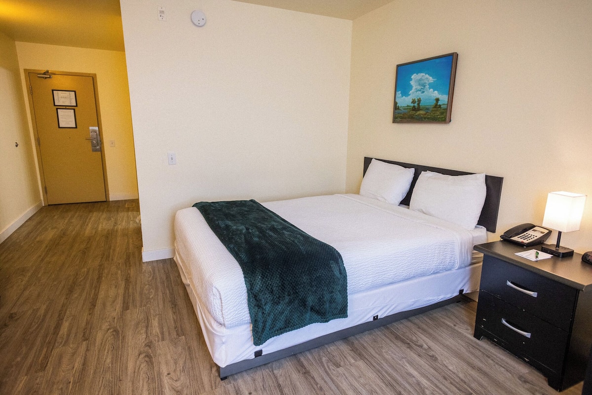 A hotel room with a bed, a nightstand, a lamp, a painting on the wall, and a door.