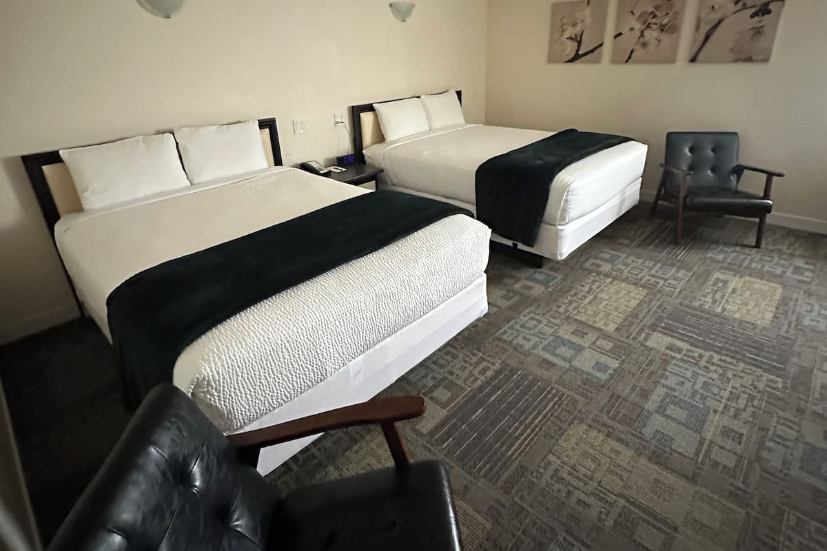 A hotel room with two beds, a chair, a ceiling fan, and artwork on the wall.