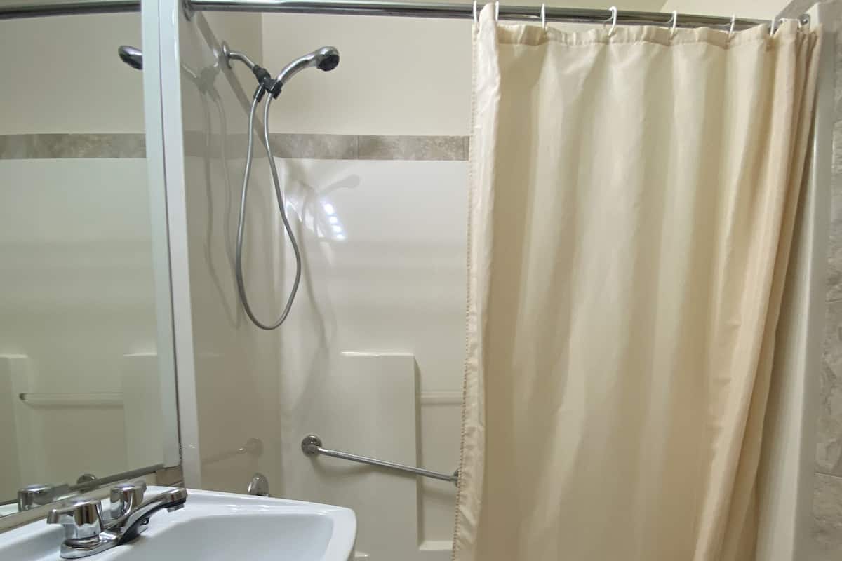 A bathroom with a sink, mirror, shower, and a towel rack.