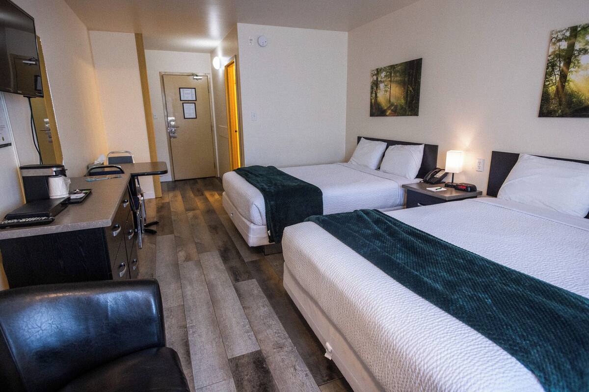 A hotel room with two beds, a desk with a chair, a small table, and a TV.