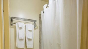 A bathroom with a toilet, a towel rack with towels, a shower curtain, and a trash can.