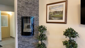 A hallway with a stone accent wall, a framed landscape painting, and two potted plants. - Sleep Suite Motel (Steinbach)