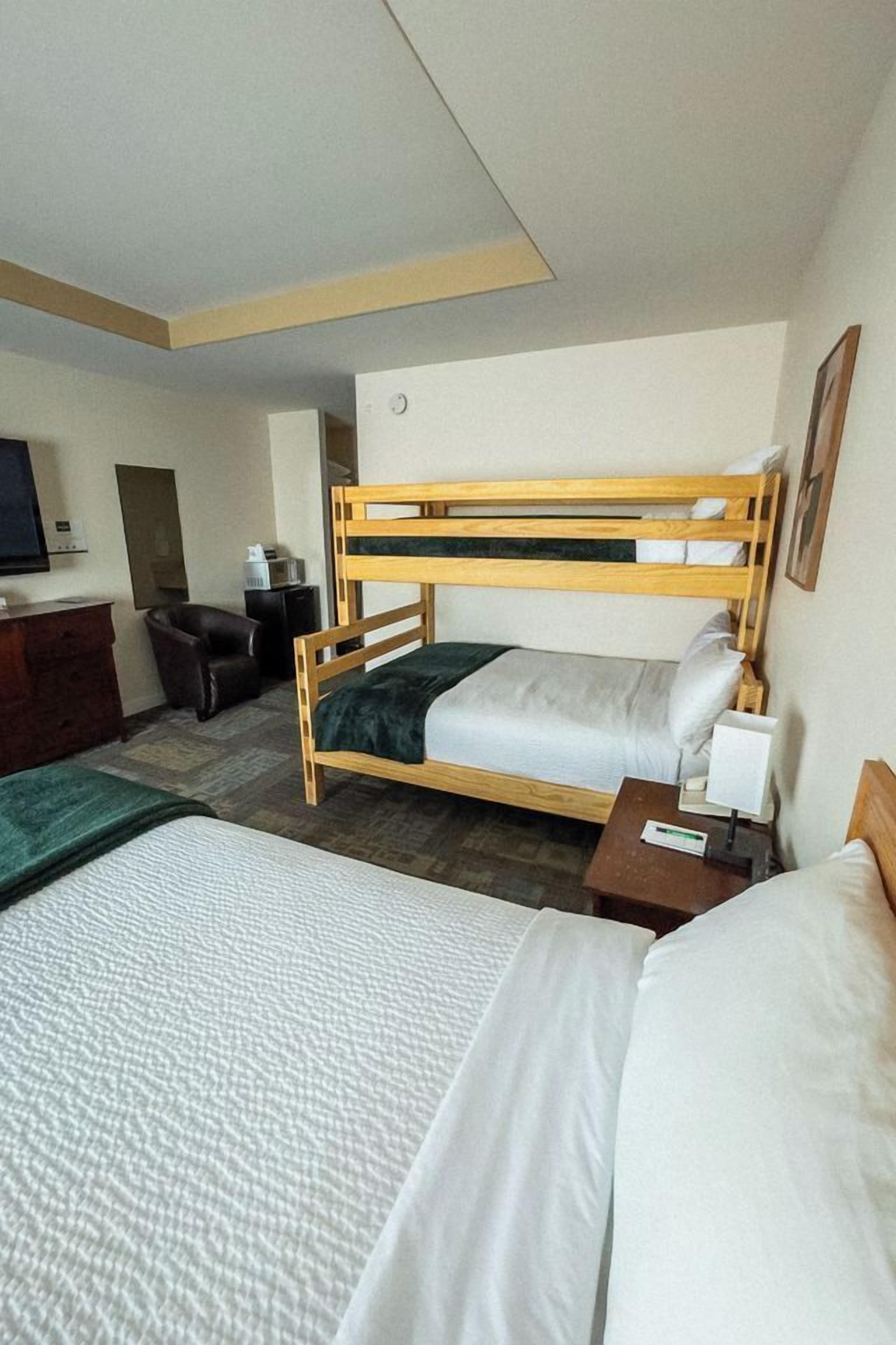 A hotel room with two beds, a desk, a chair, a television, and a small table with a lamp.