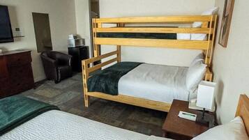A hotel room with two beds, a desk, a chair, a television, and a small table with a lamp.