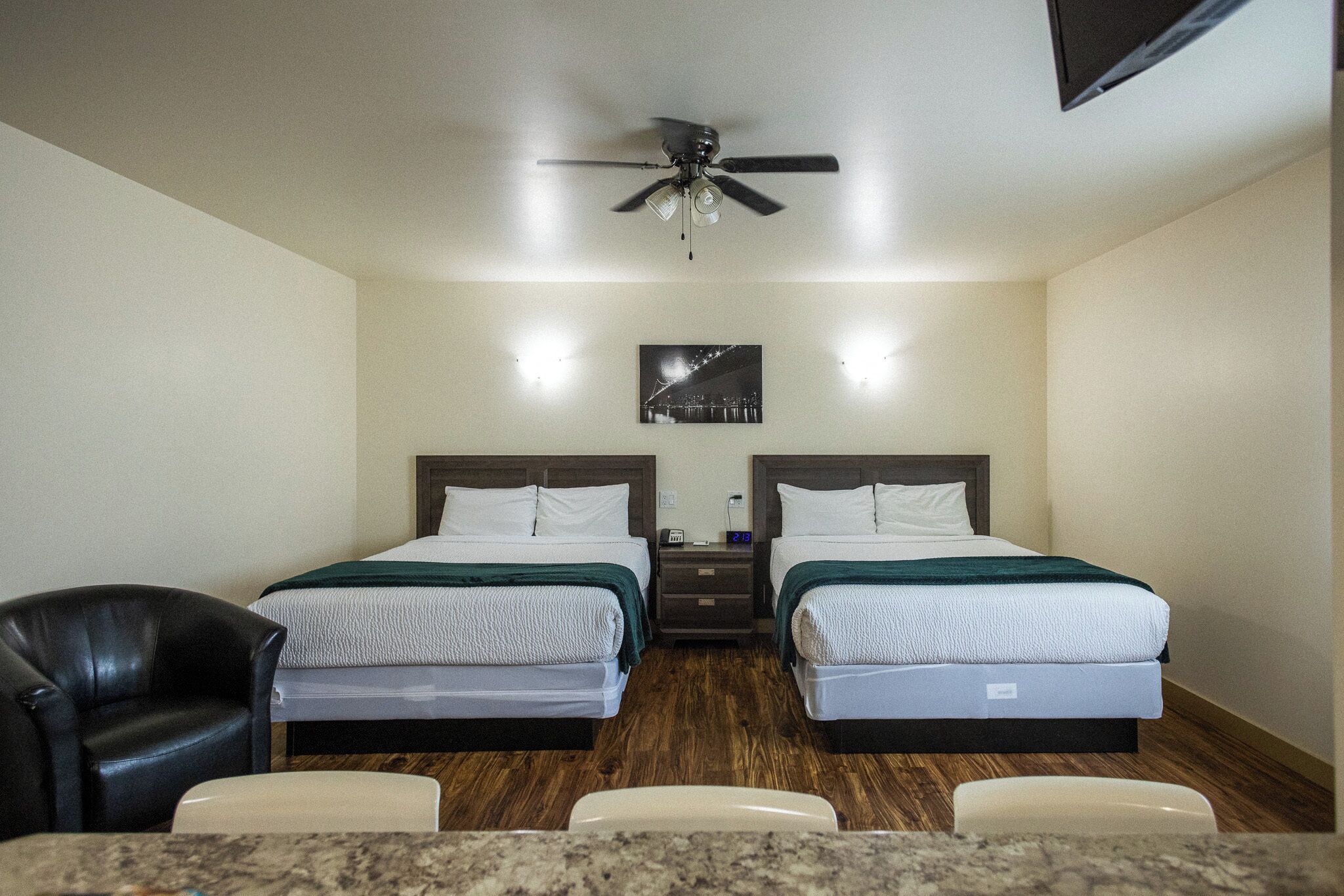 A hotel room with two beds, a ceiling fan, a nightstand, a chair, and a TV.