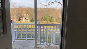 A wooden deck with a white railing, leading to a view of a barn and trees. - Bright and Serene Country Cottage in the Blue Ridge Mountains (Hillsville)