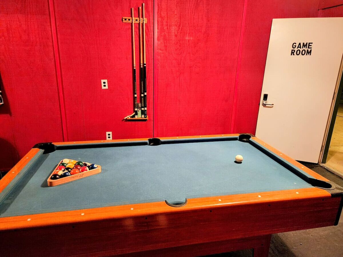 Une table de billard avec un mur rouge et une porte portant l’inscription « SALLE DE JEUX ».
