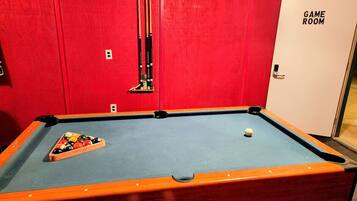 Une table de billard avec un mur rouge et une porte portant l’inscription « SALLE DE JEUX ».