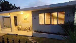Una casa moderna con un patio, un letrero de bienvenida y una ventana con persianas.