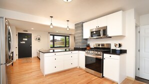 A modern kitchen with white cabinets, stainless steel appliances, and a wooden floor. - Beautiful newly remodeled house .5 miles to Lambeau/Resch center. (Pet Friendly) (Green Bay)