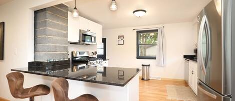 A modern kitchen with a central island, bar stools, stainless steel appliances, and a large refrigerator.