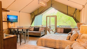 A tented accommodation with a dining area, a TV, and a bed with patterned bedding. - Rare Find! New waterfront Cabin with kayaking, hiking, pools & hot tub! SG25 (Marion)