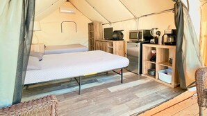 Un hébergement confortable en forme de tente, comprenant un lit, un coin cuisine et un fauteuil en osier.