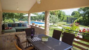 An outdoor patio with a dining table, chairs, and a sofa with cushions. There is a pool visible in the background. - Secluded vacation house surrounded by nature (Žminj)