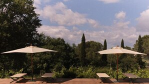 Een zwembadgedeelte met twee ligbedden en twee grote parasols, omringd door weelderige begroeiing en hoge bomen.