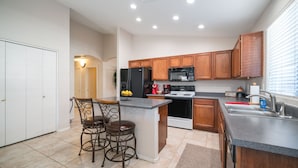 A modern kitchen with wooden cabinets, a black refrigerator, a microwave, and a sink. There are two bar stools and a small island with a bowl of lemons. - Cozy 3BR, 2BA house in a quiet, gated Alta Mesa Community. (Mesa)