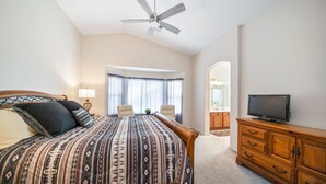 A bedroom with a bed, a TV, a ceiling fan, and a view of the bathroom. - Cozy 3BR, 2BA house in a quiet, gated Alta Mesa Community. (Mesa)