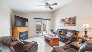 A living room with leather sofas, a flat-screen TV, a fireplace, a ceiling fan, and a sliding glass door leading to an outdoor patio. - Cozy 3BR, 2BA house in a quiet, gated Alta Mesa Community. (Mesa)