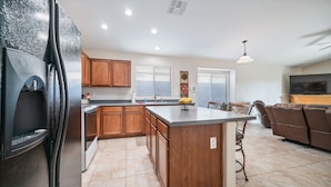A modern kitchen with wooden cabinets, a central island, and a dining area with a sofa and chairs. - Cozy 3BR, 2BA house in a quiet, gated Alta Mesa Community. (Mesa)