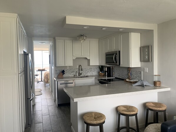A modern kitchen with white cabinetry, a central island with stools, stainless steel appliances, and a chandelier.