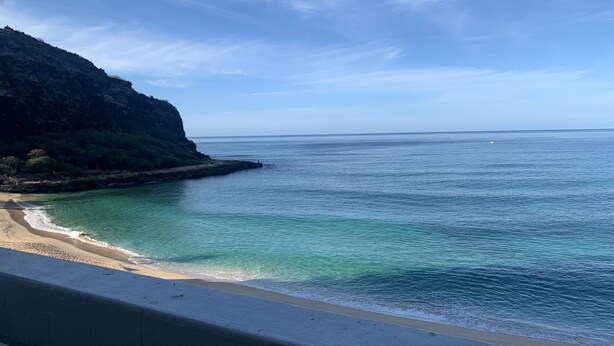 Blick auf die Küste mit klarem türkisblauem Wasser, einem Sandstrand und einer felsigen Klippe.