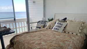 Ein Schlafzimmer mit Bett, Kissen, einem Nachttisch und Meerblick durch eine Schiebetür.