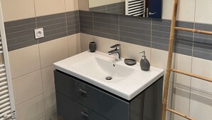 A modern bathroom with a white sink, dark cabinets, and a mirror above it. - Cosy apartment rental (SANTA LUCIA DI MORIANI)