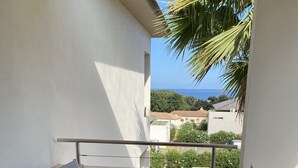 A balcony with a glass table and white chairs, overlooking a residential area and the sea. - Cosy apartment rental (SANTA LUCIA DI MORIANI)