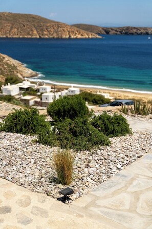A coastal landscape with white buildings, a pebble path, and a view of the sea and hills.