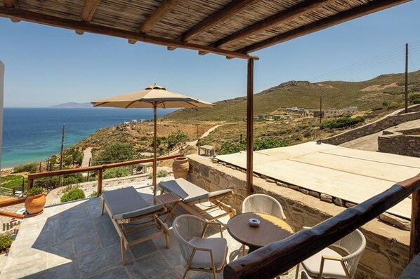 A terrace with lounge chairs, a table, and a view of the sea.