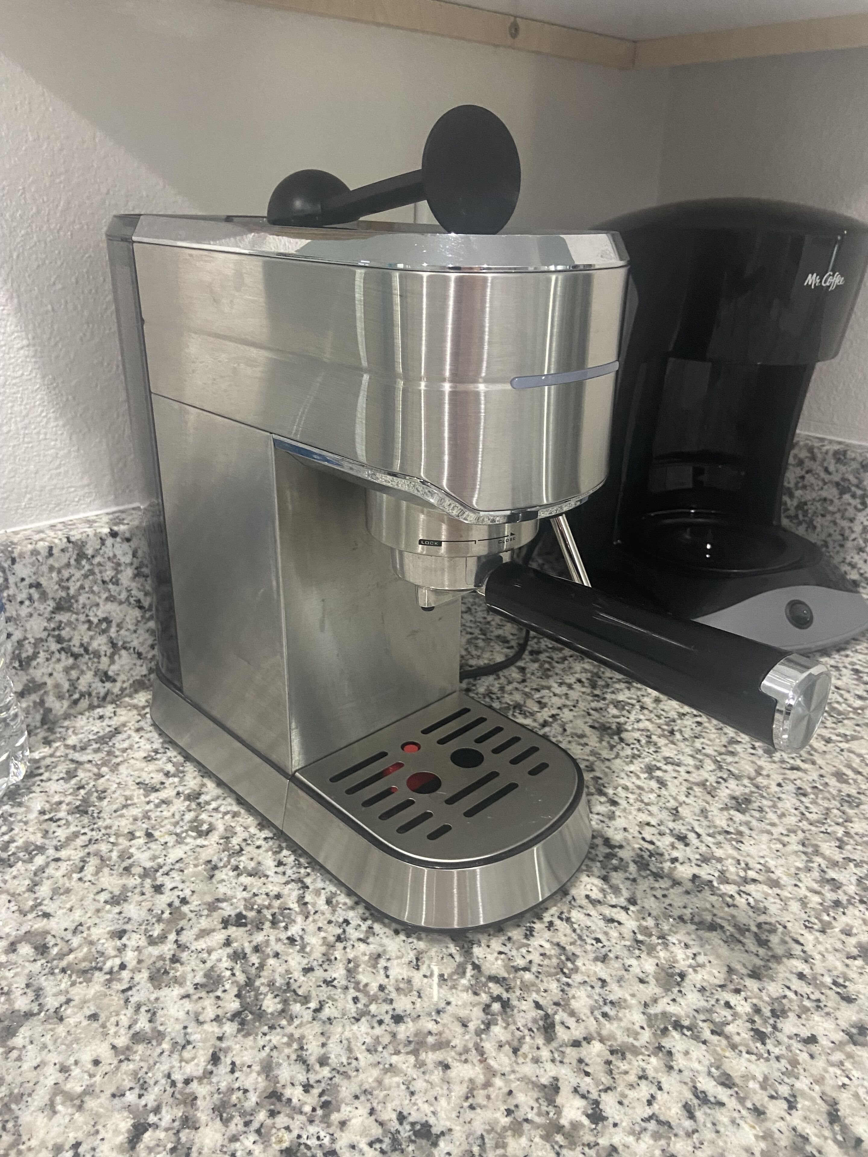 Eine Kaffeemaschine aus Edelstahl mit Auffangbehälter und Kaffeekanne auf einer Granitabdeckung.