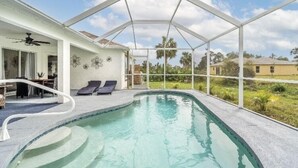Un espace piscine doté d’une structure en verre, de chaises longues et d’un ventilateur de plafond.
